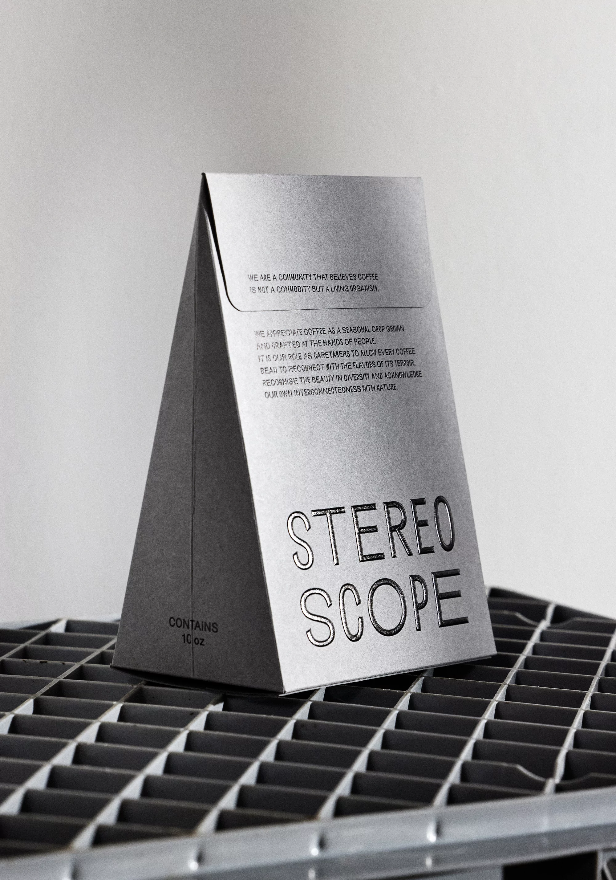 Pyramid-shaped Stereoscope coffee bag sits on a metal grate surface. The bag has visible text and sits in front of a plain white background.