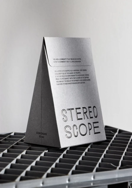 Pyramid-shaped Stereoscope coffee bag sits on a metal grate surface. The bag has visible text and sits in front of a plain white background.