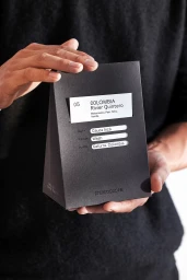 Person holding a black matte coffee bag with white informational label for Stereoscope brand identity