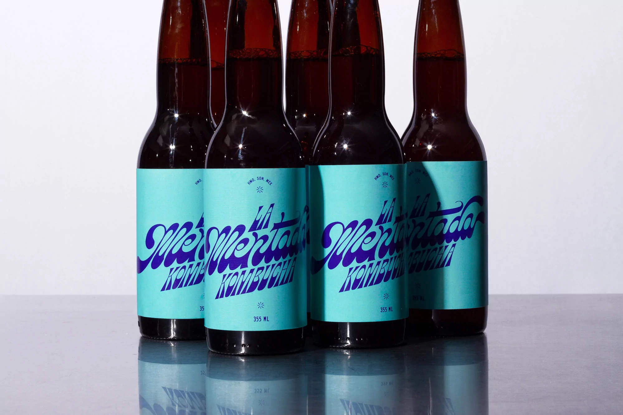 Multiple amber kombucha bottles with teal labels and blue writing create a refreshing and visually appealing composition on a gray surface.