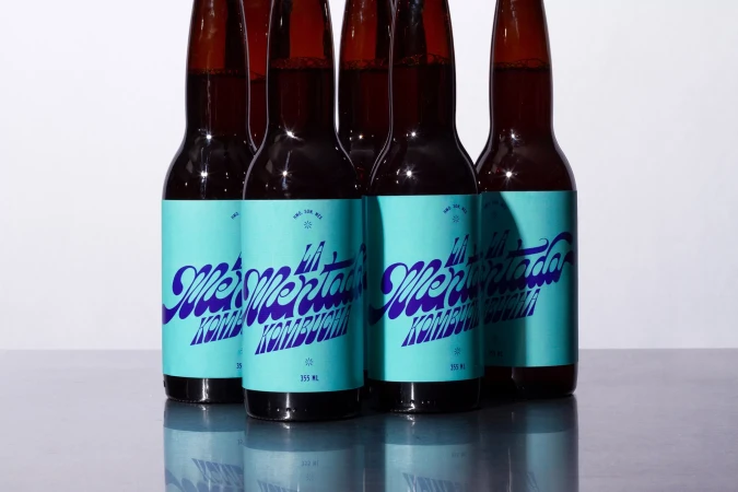 Multiple amber kombucha bottles with teal labels and blue writing create a refreshing and visually appealing composition on a gray surface.