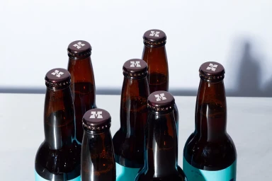 Close-up view of amber glass bottles with printed bottle caps against a white surface, showcasing the Mentados brand identity.