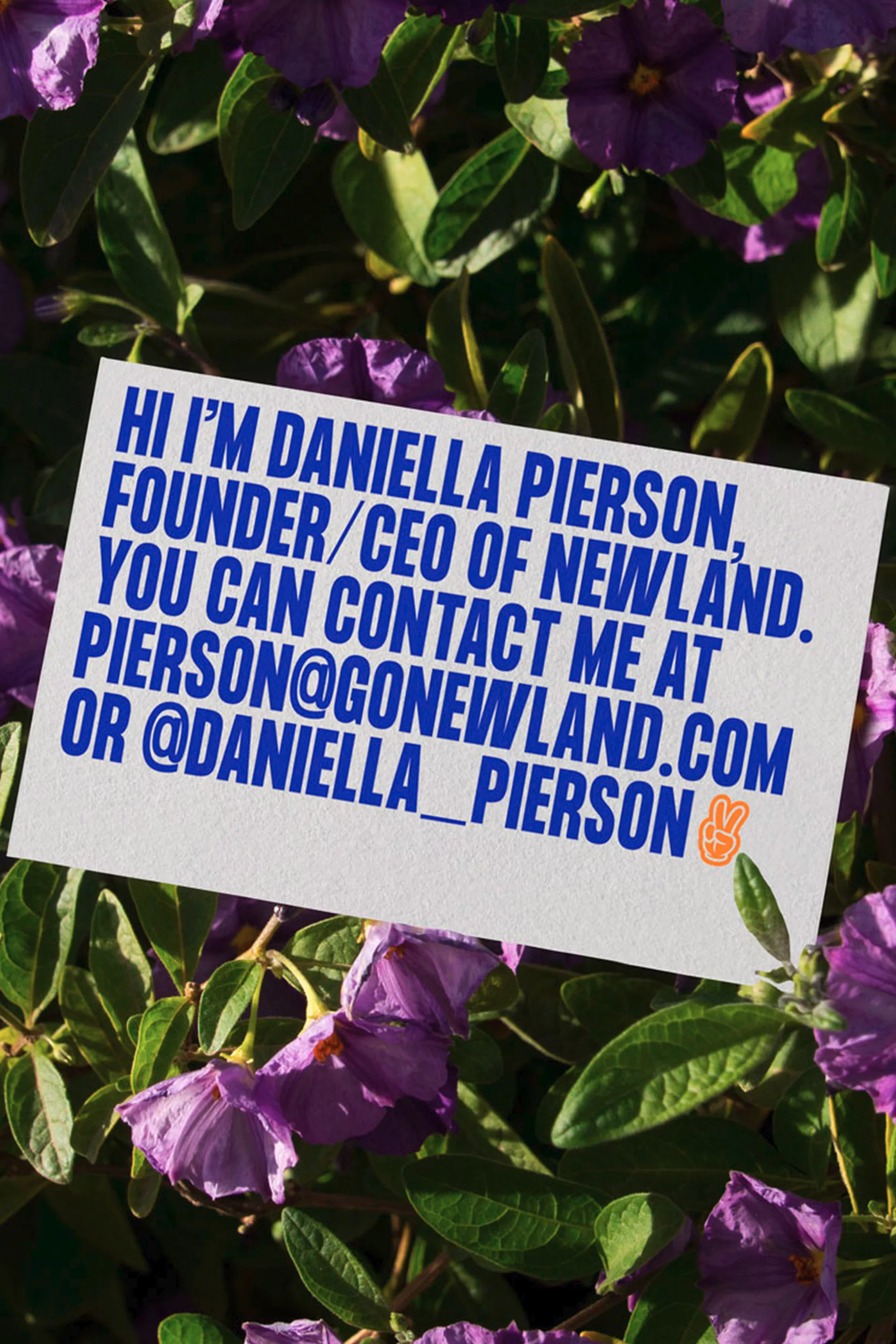 Close-up of a business card in a bed of purple flowers and green leaves, showcasing the name and contact information of Daniella Pierson.