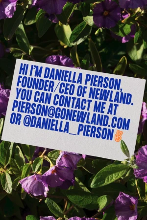 Close-up of a business card in a bed of purple flowers and green leaves, showcasing the name and contact information of Daniella Pierson.