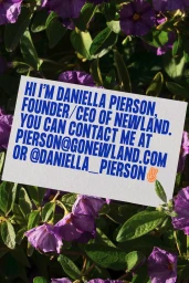 A white business card with blue text resting amidst vibrant purple flowers and green foliage.