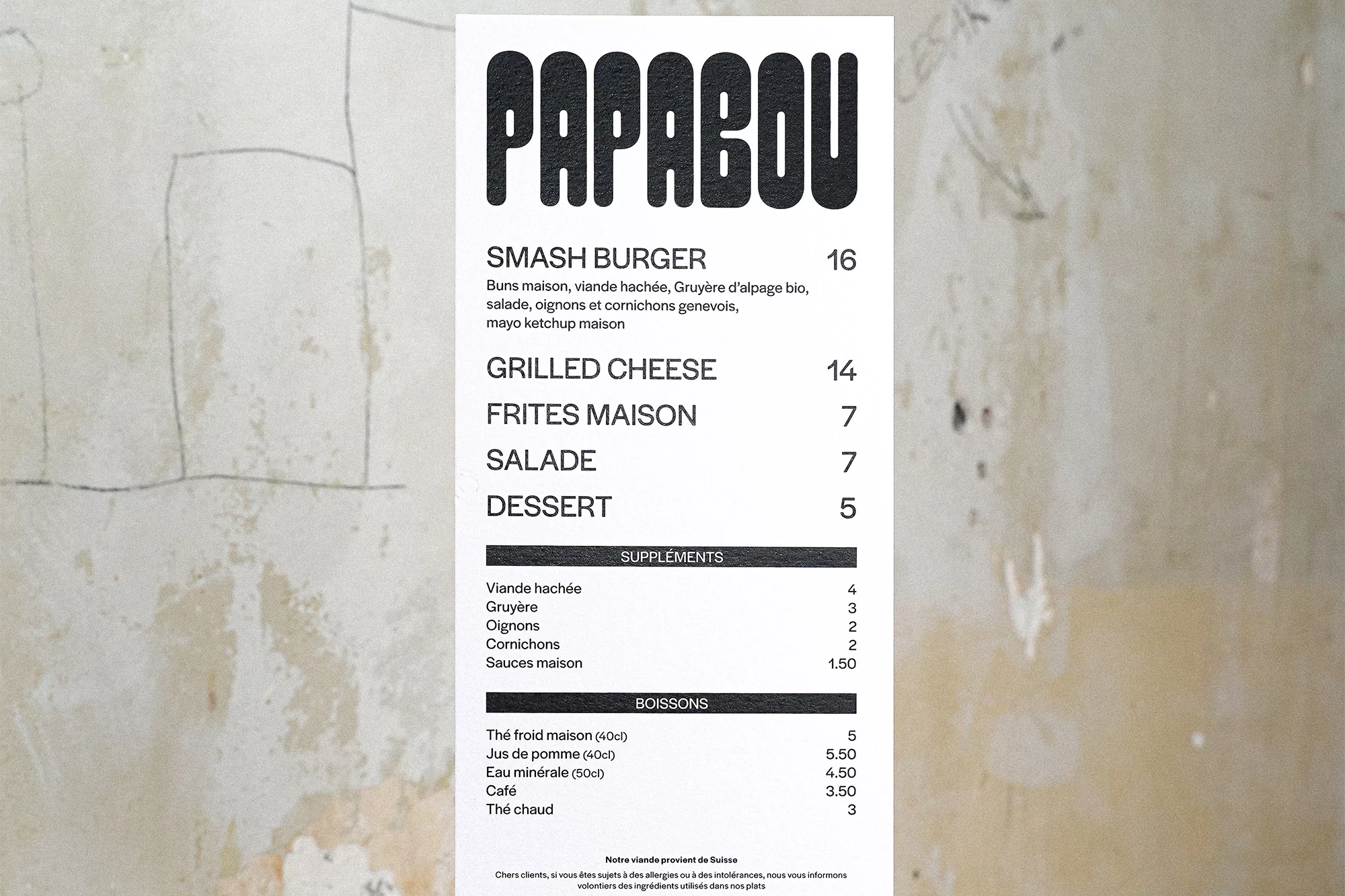 A menu for Papabou restaurant featuring smash burger, grilled cheese, frites maison, salade, and dessert on a textured wall.