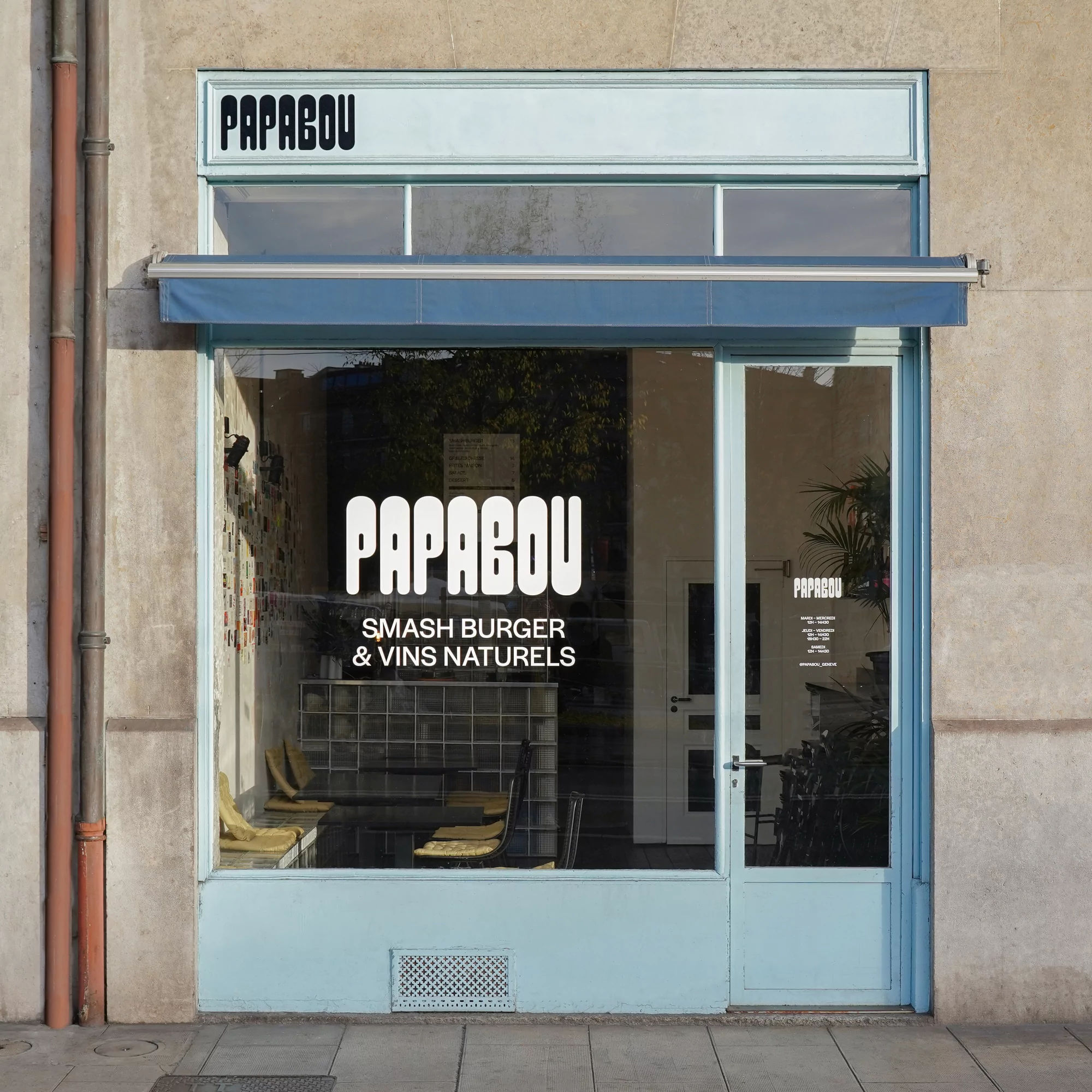 Exterior daytime view of Papabou restaurant front featuring a window display with logo and menu against a gray concrete building.