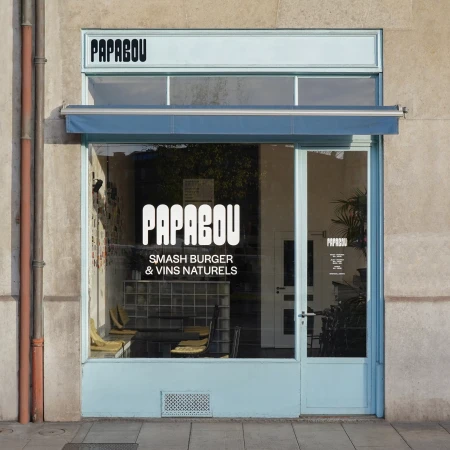 Exterior daytime view of Papabou restaurant front featuring a window display with logo and menu against a gray concrete building.