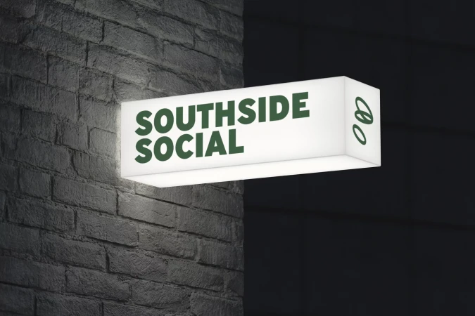 Illuminated sign reading 'Southside Social' mounted on a textured grey brick wall, casting a warm glow in a dimly lit environment.