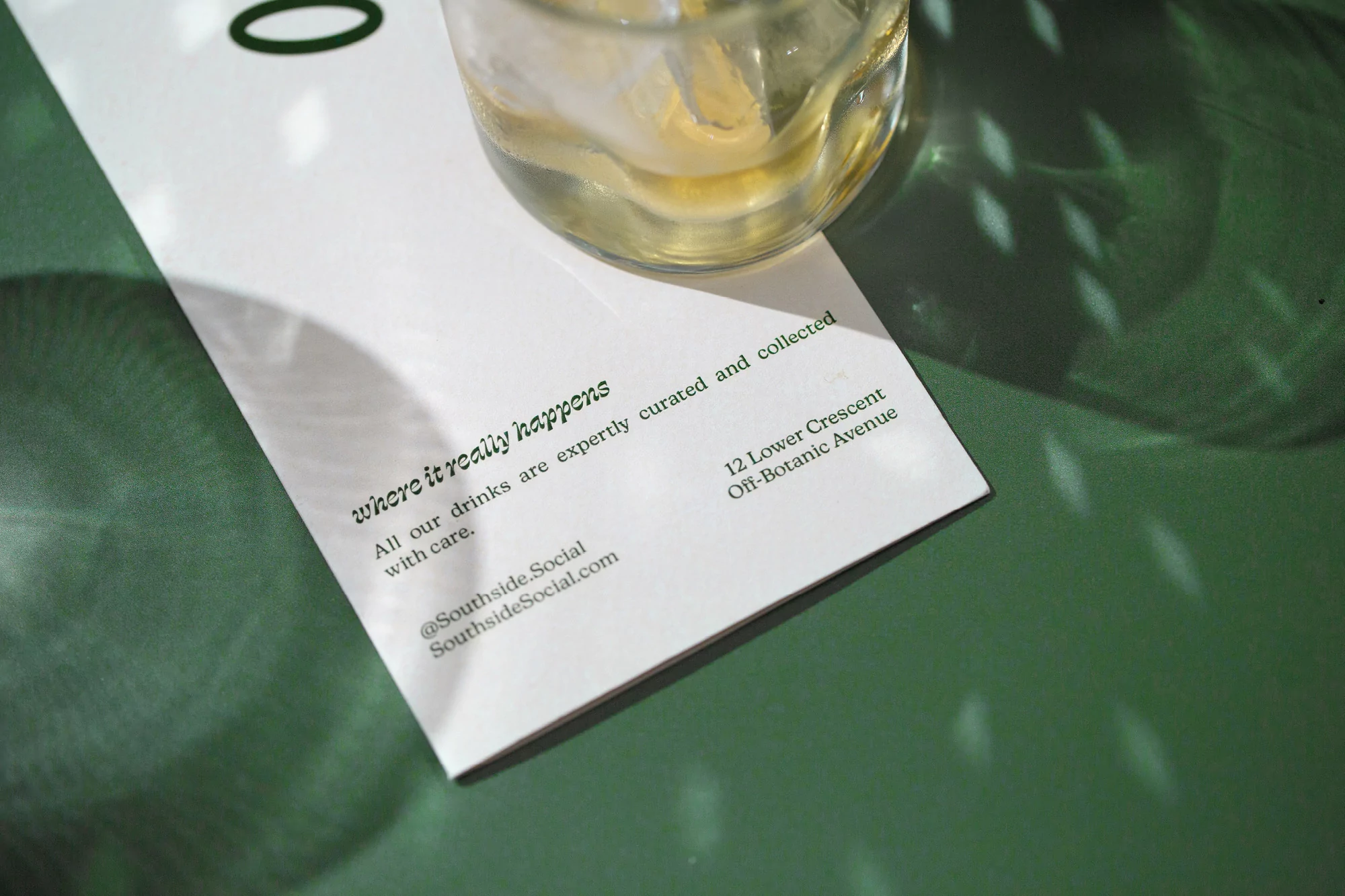 Close-up of a drink with ice on a white card on a green surface with window-shadows, showcasing a refreshment and modern design.