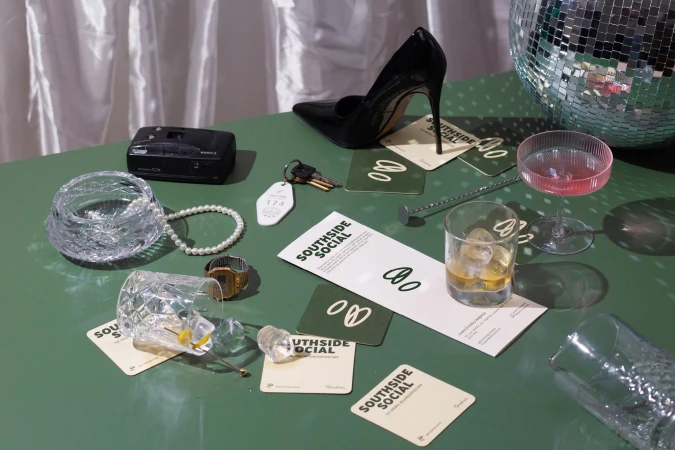 Still life on a green table featuring a disco ball, high heel, drinks, and vintage accessories.
