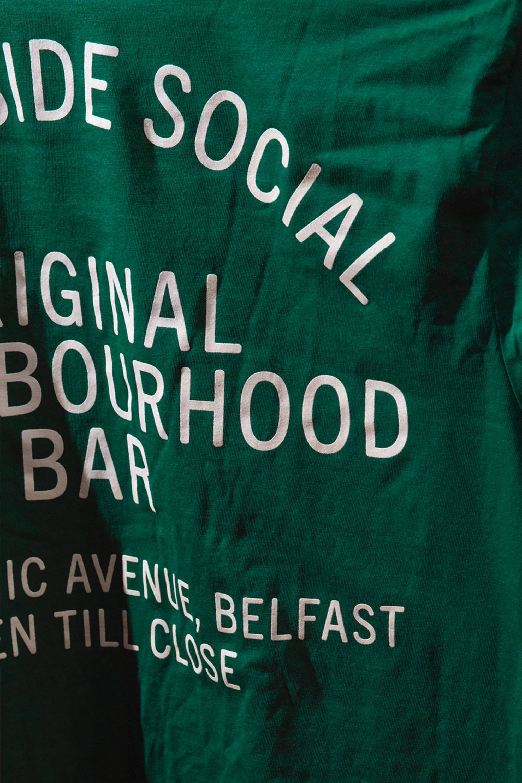 Text on a dark green fabric reads 'Side Social Original Neighbourhood Bar,' an advertisement for a local Belfast establishment.