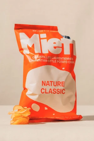 Orange and white bag of Miel Nature Classic Laurentian-Style Potato Chips with a stack of potato chips on a light surface.