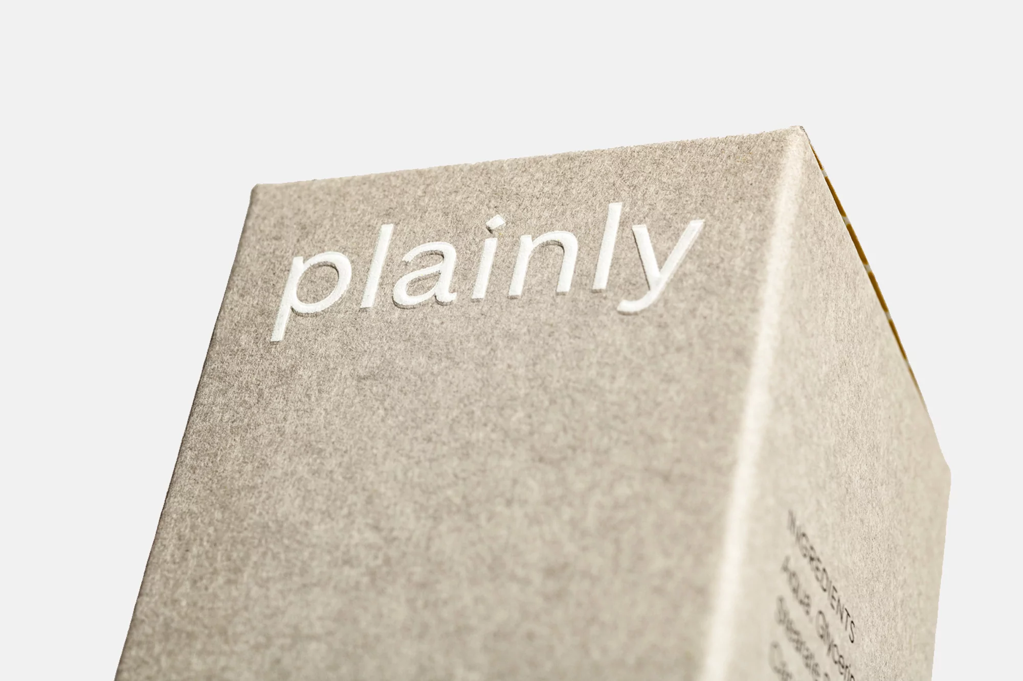 Close-up of a textured, light-gray box with the word 'plainly' in white embossed lettering on a white background.