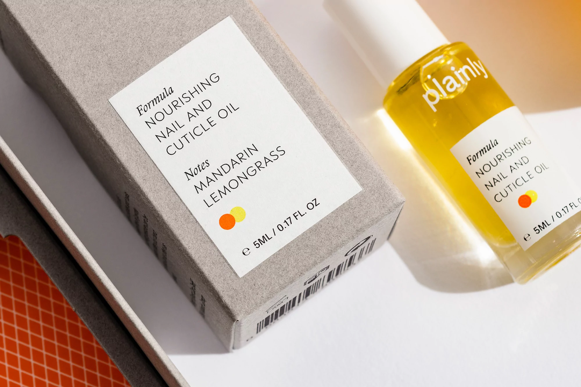 Close-up of Plainly brand nourishing nail and cuticle oil in a clear bottle, next to the product box with mandarin lemongrass notes.