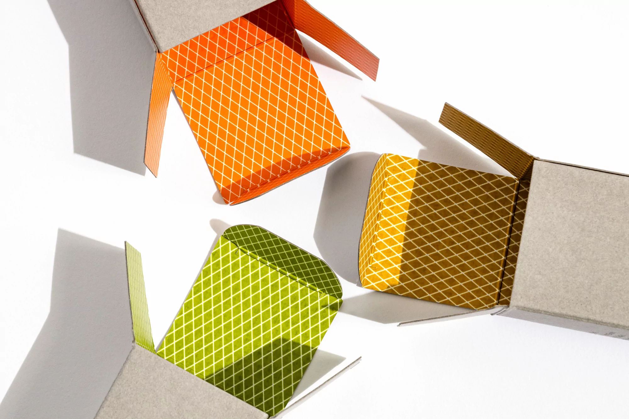 Three open cardboard boxes with patterned interiors in orange, green, and brown on a white surface casting shadows.