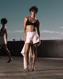 Model wearing a black crop top and white shorts on a rooftop under a clear sky for Collection 02 by Deering.