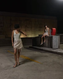 Two women in shimmering fringed outfits standing in a concrete parking structure at night