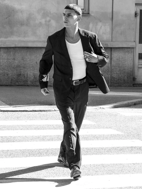 Young man in a pinstripe suit walks across a zebra crosswalk on a city street, captured in black and white with natural light.
