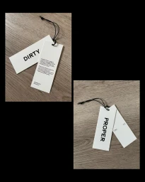Two white rectangular hang tags with black typography and black string resting on a wooden surface