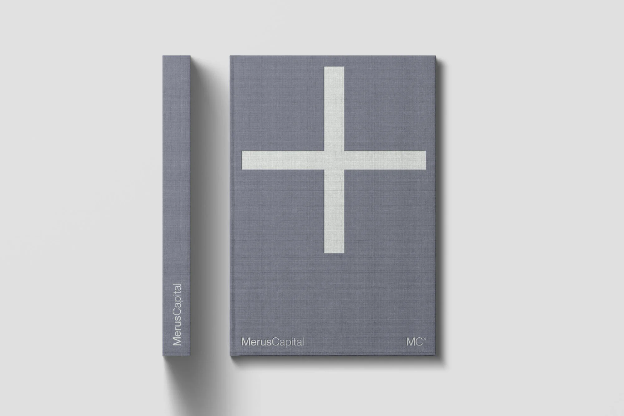 Two hardcover books, gray with a large white plus sign, rest on a clean white surface in a minimalist composition.