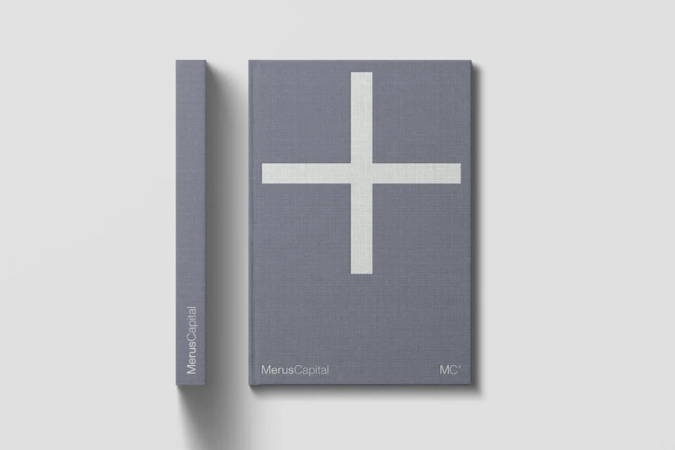 Two hardcover books, gray with a large white plus sign, rest on a clean white surface in a minimalist composition.