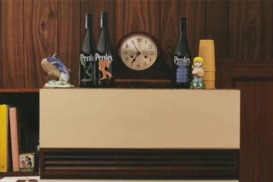 Penley wine bottles displayed on a cabinet shelf with a vintage clock and retro figurines against wood paneling