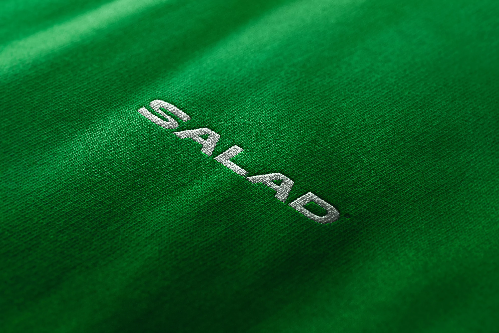 Close-up of a bright green fabric with a diagonal pattern and the white embroidered text 'SALAD' running across the material.