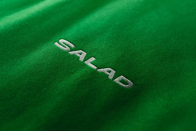 Close-up of a bright green fabric with a diagonal pattern and the white embroidered text 'SALAD' running across the material.