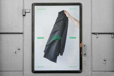 Hand holding up a dark garment on a poster inside a metallic display case with green typography for Salad brand identity.