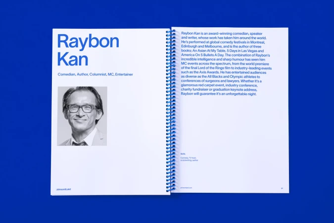 Raybon Kan portrait on an open book, showcasing his titles: Comedian, Author, Columnist, MC, Entertainer, against a solid blue backdrop.
