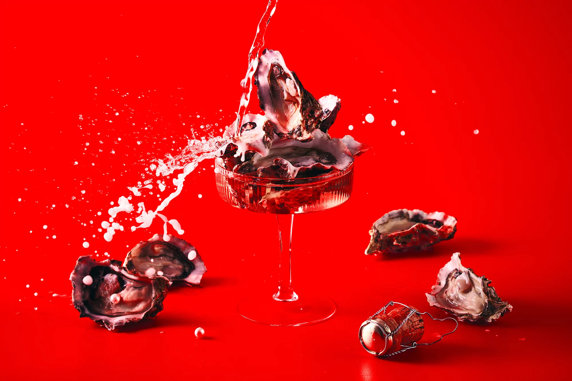 Oysters on ice in a champagne coupe glass with a splash of liquid against a red background for fine dining or culinary advertising.