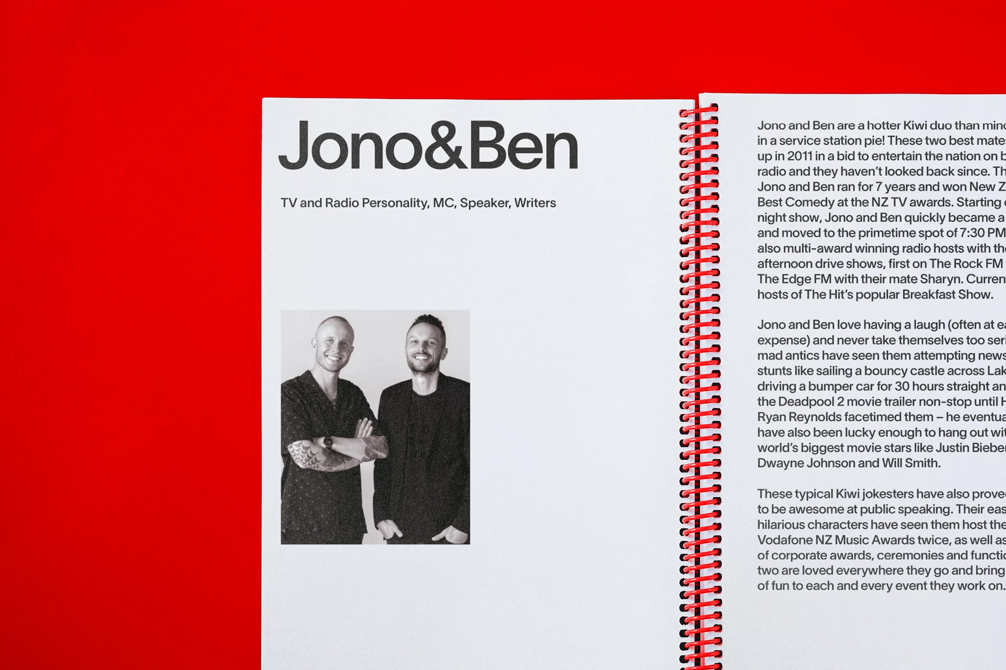 Two adult males, Jono and Ben, stand side-by-side smiling slightly in a promotional image on a page in a notebook with red binding.
