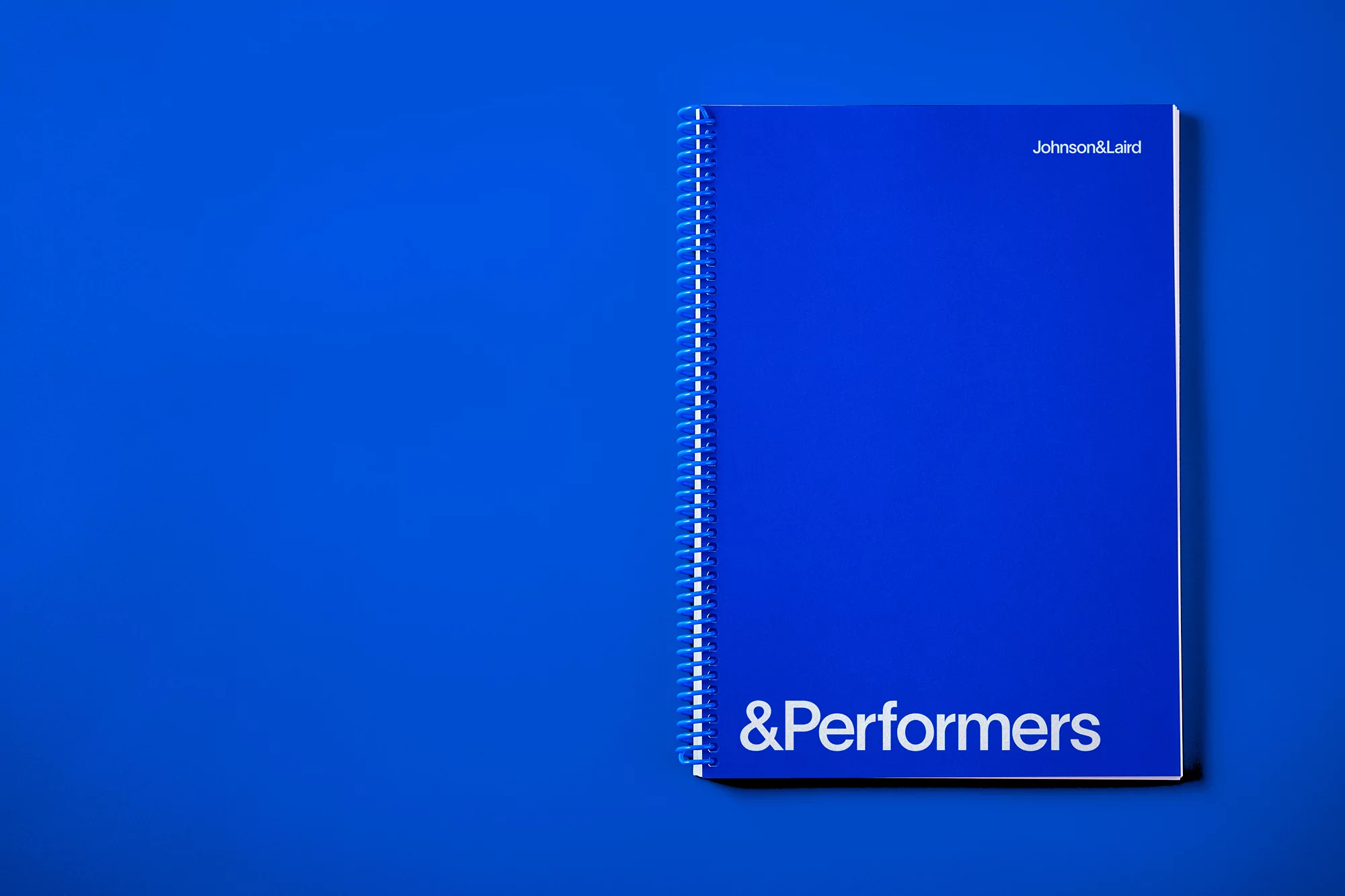 Bright blue notebook with white spiral binding displays the words Johnson&Laird at the top and &Performers on a saturated blue background.