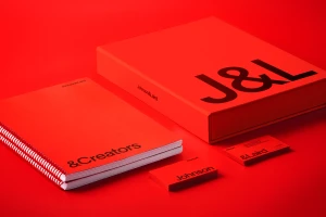 Red brand identity collateral including a spiral-bound notebook, a large branded box, and business cards on a red surface.