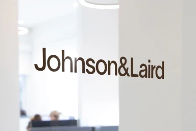Brown Johnson and Laird company logo lettering displayed on a clean white office wall with blurred workspace in background