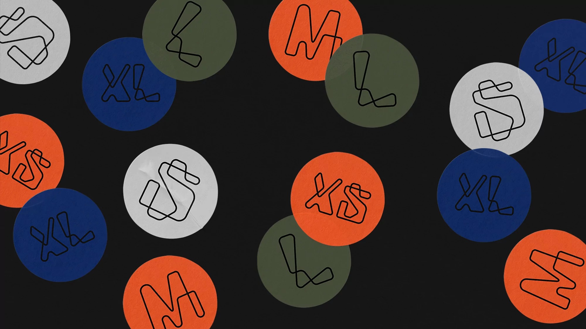 Abstract circles with clothing size initials in shades of orange, grey, green, and blue against a dark grey background in flat lay.