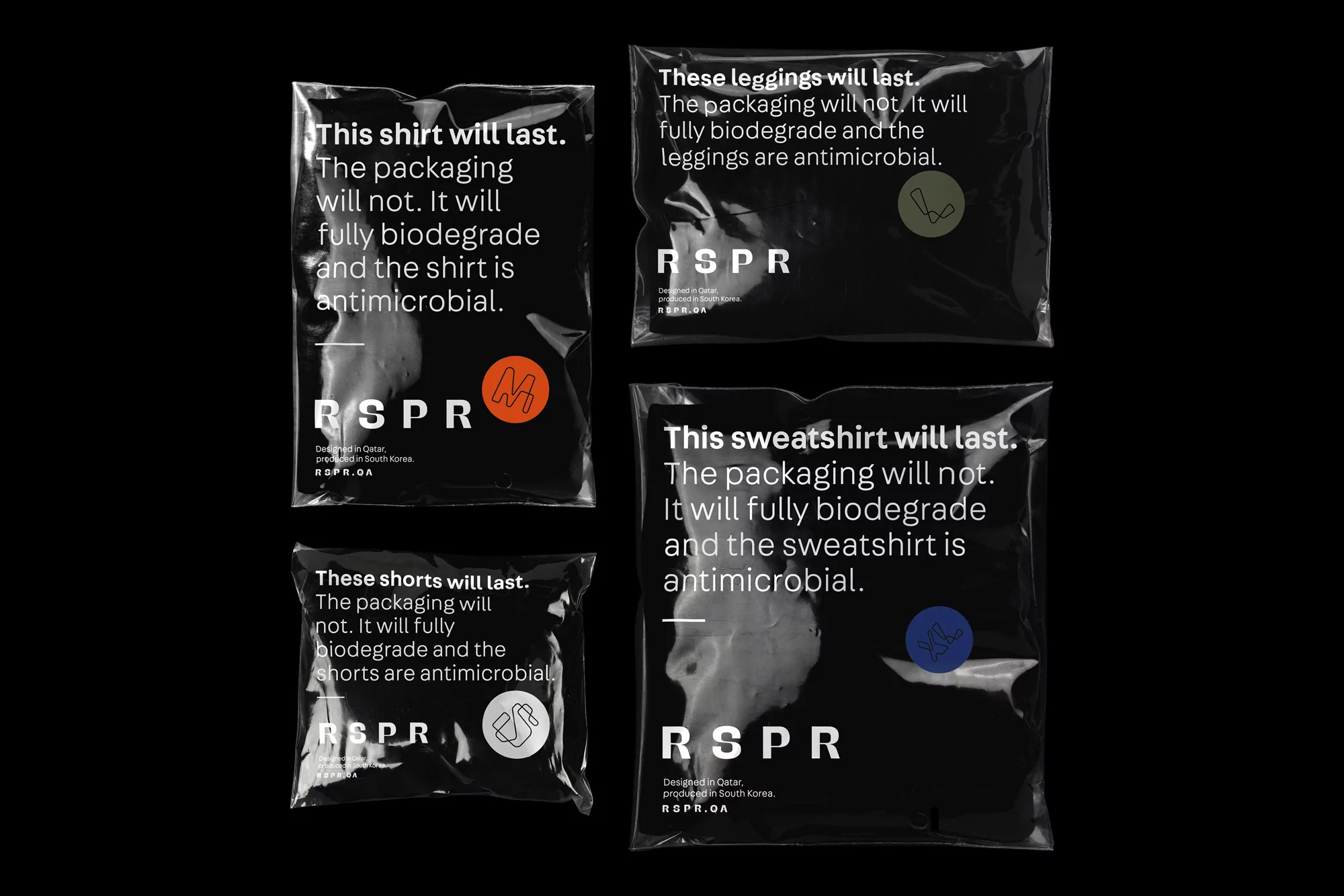 Four dark, glossy packages display apparel branding, each containing garments and showcasing minimalist design against a stark black backdrop.