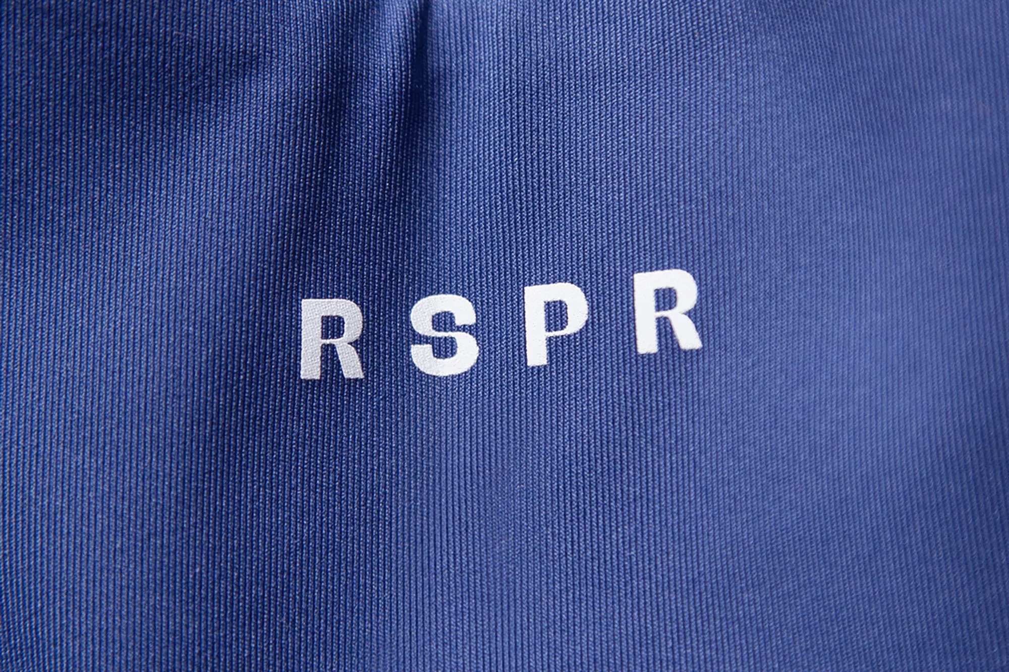 Close-up of blue textured fabric with the white letters RSPR centered horizontally and stacked vertically on the surface.