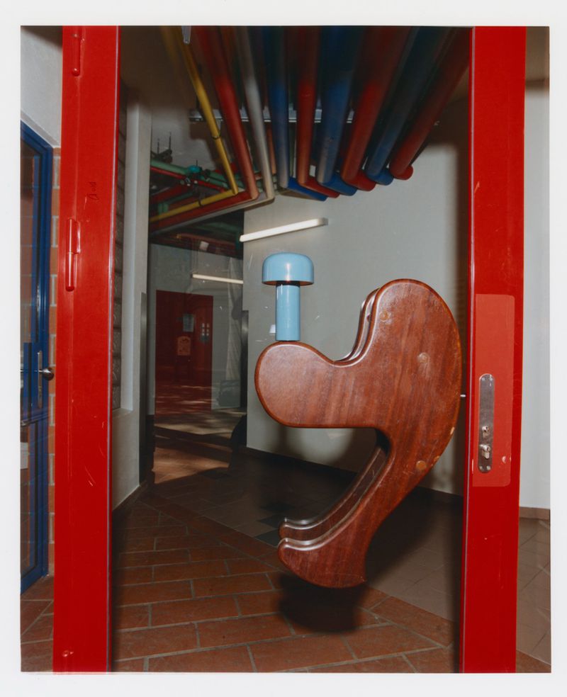Indoor shot of an elaborate, colorful children's climbing structure and play area with red support beams and brick floors in a hallway.