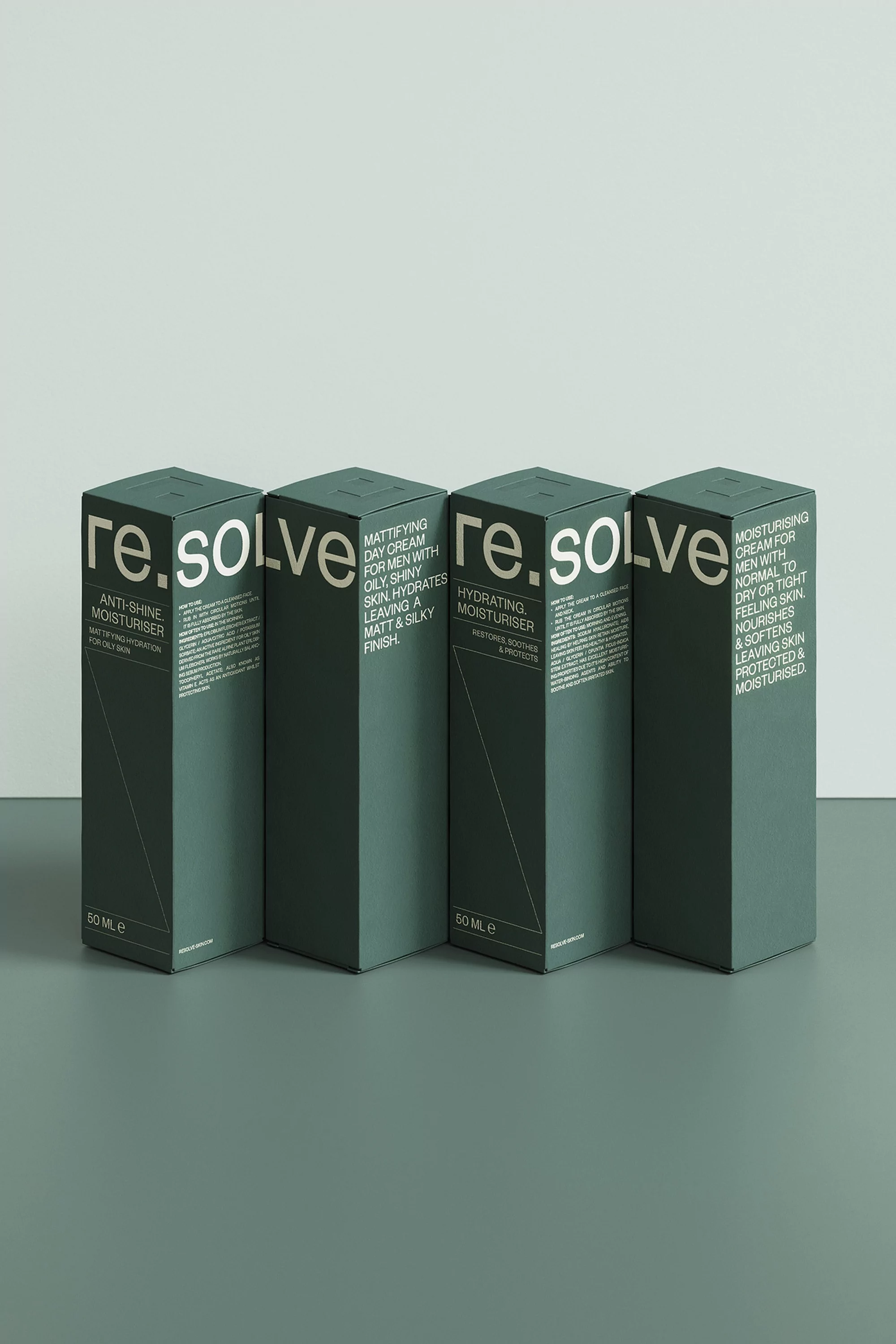 Four dark green boxes of re.solve moisturizer stand in a row against a pale gray backdrop in a product photography studio setting.