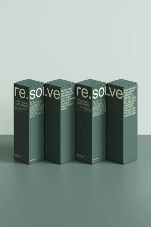Four dark green boxes of re.solve moisturizer stand in a row against a pale gray backdrop in a product photography studio setting.