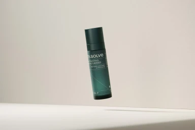 A dark green cylindrical moisturiser bottle levitating against a neutral beige studio background.