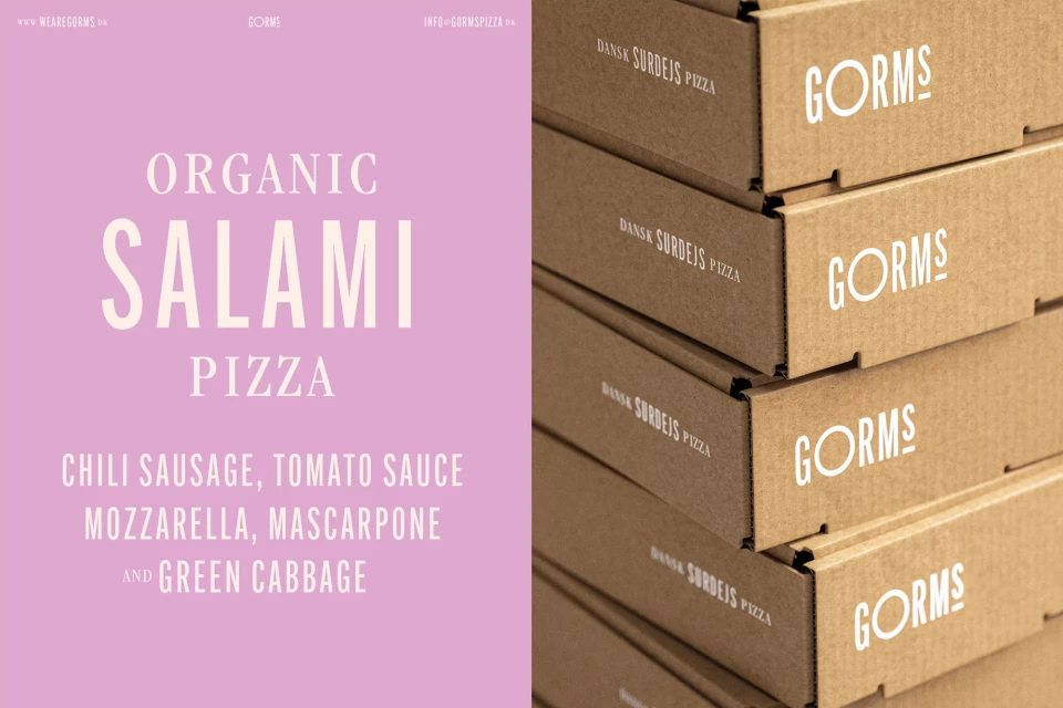 A promotional image features pizza boxes stacked against a lilac background with white text advertising organic salami pizza.