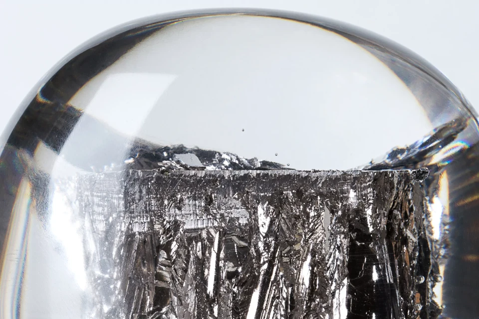 Close-up of a semi-transparent sphere encasing a dark, textured material, set against a clean, white background. Abstract image.