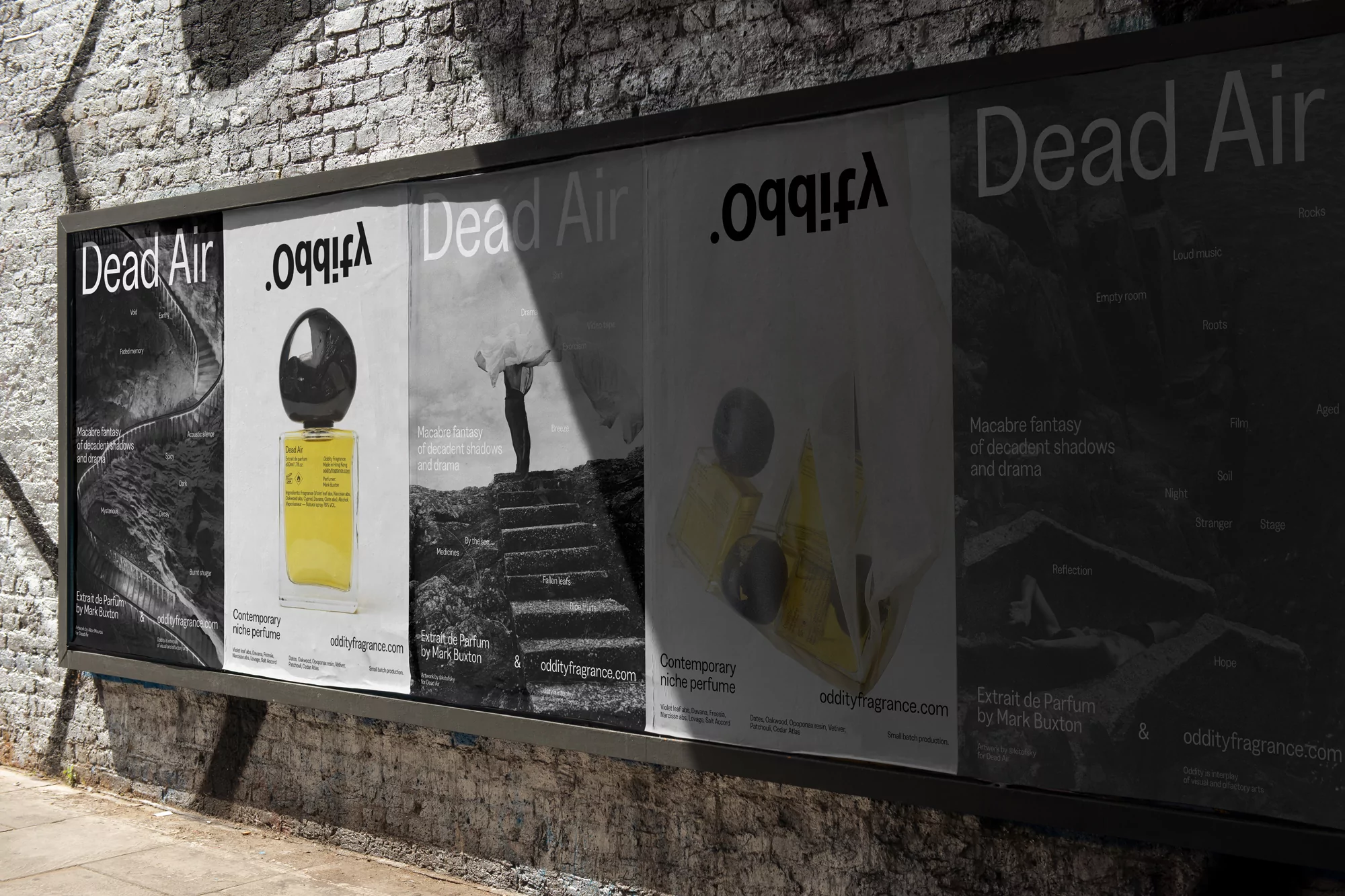 Large outdoor advertising billboard displaying multiple black and white Dead Air perfume posters on a textured brick wall.