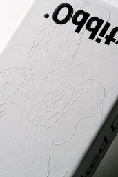 Close-up of textured white paper with embossed blind deboss line illustration and bold black typography for Oddity.