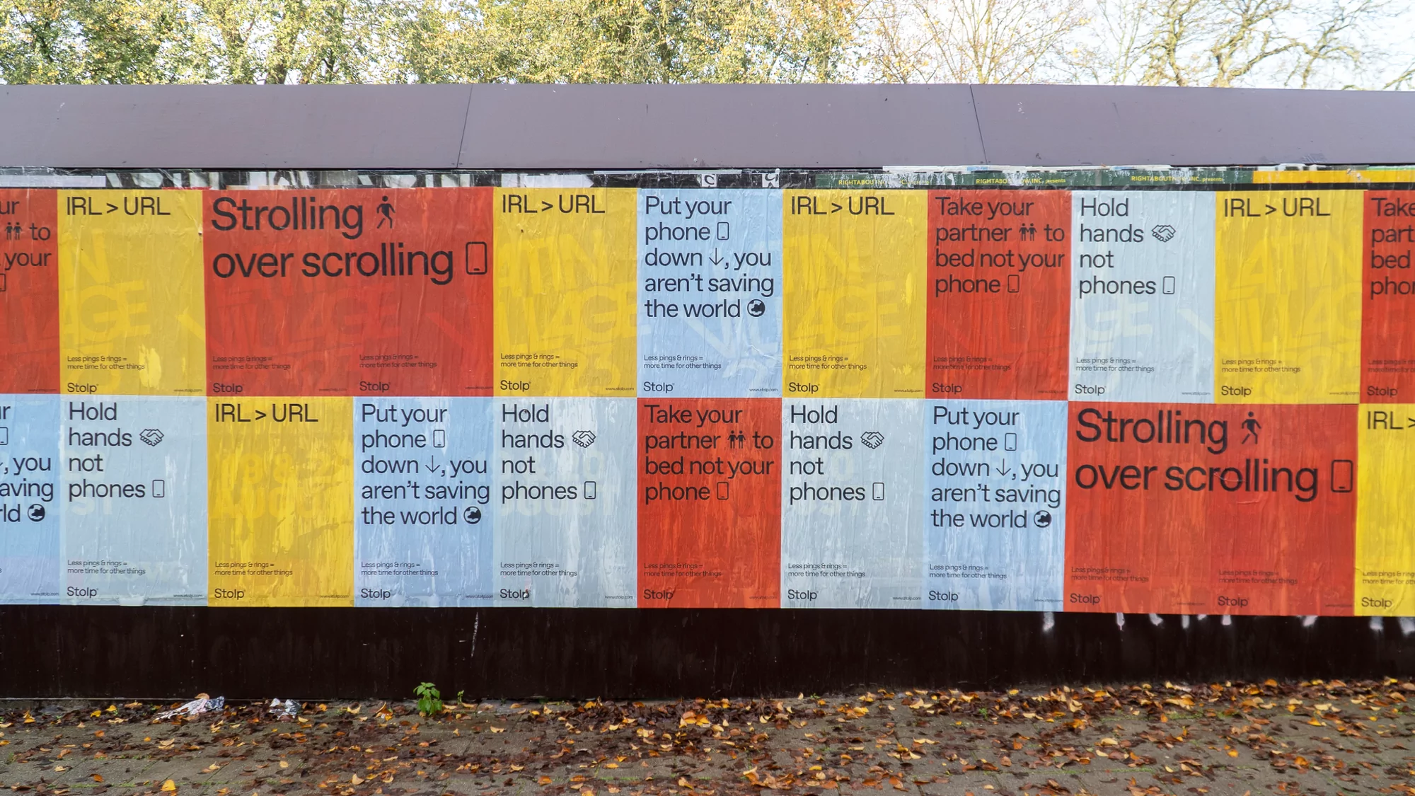 A row of posters against a dark brown wall promotes real-world experiences over phone use, with colorful designs and bold text.