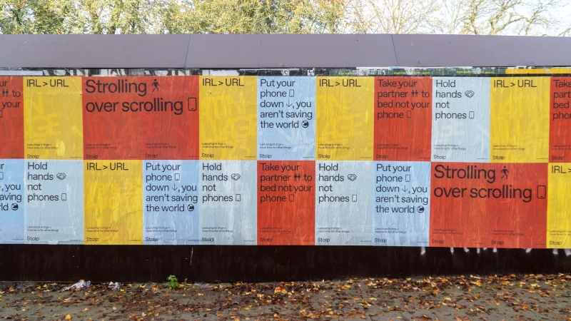 A row of posters against a dark brown wall promotes real-world experiences over phone use, with colorful designs and bold text.