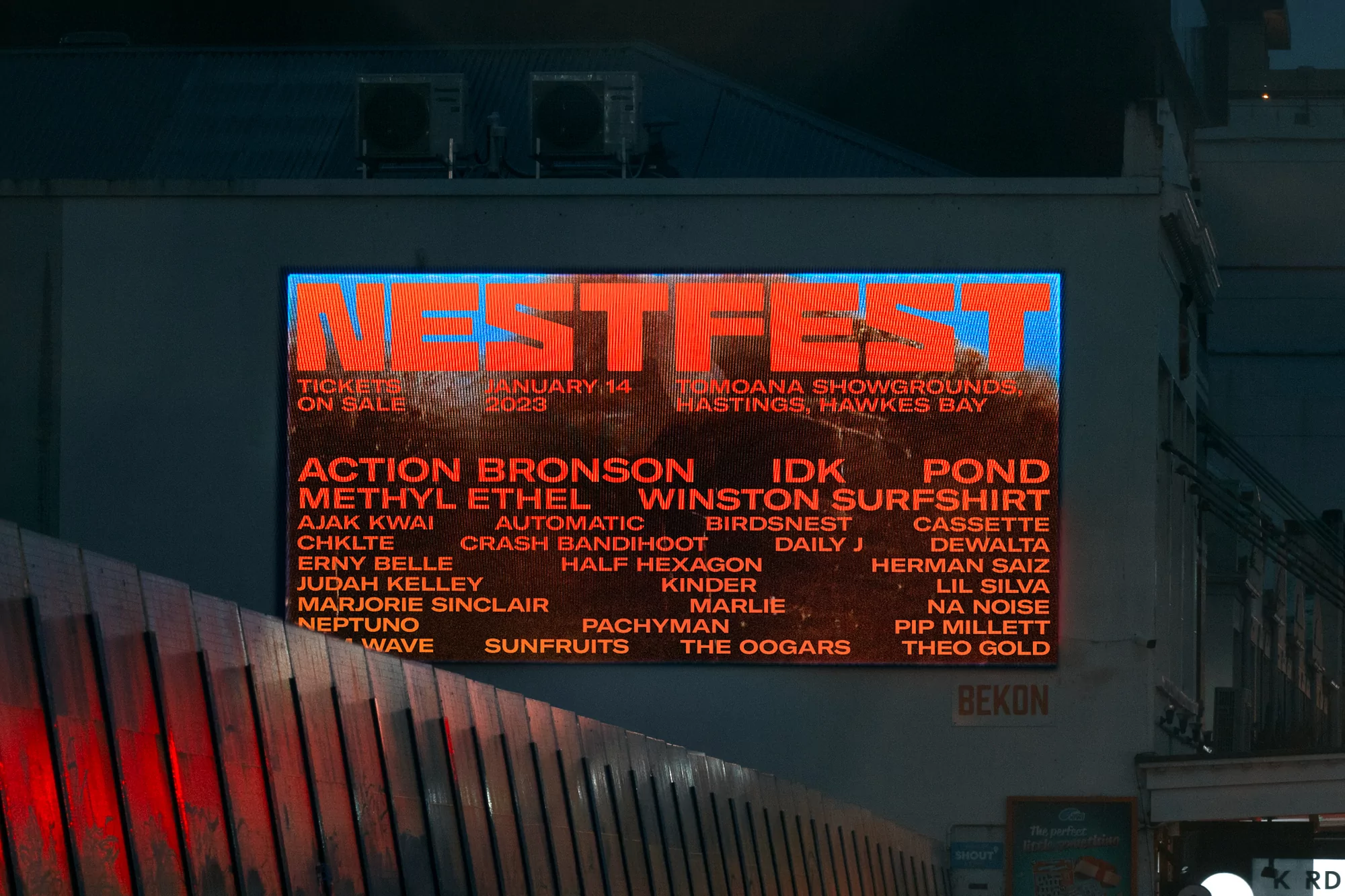 Illuminated sign for 'Nestfest' music festival displays lineup and ticket information on the side of a building at night.